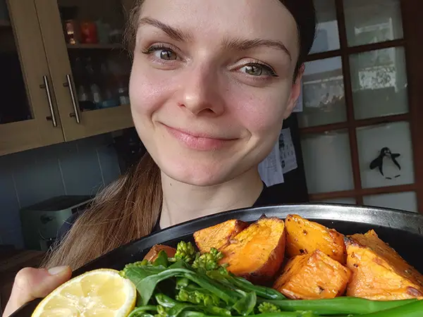 Woman with a plate with baked salmon, sweet potatoes and tenderstem broccoli