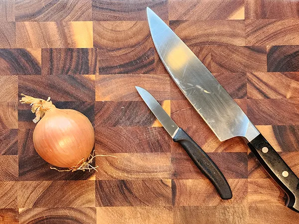 onion and two knifes on a wooden board
