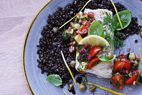 Cod fish filet on the plate with black bulgur and fresh vegetables
