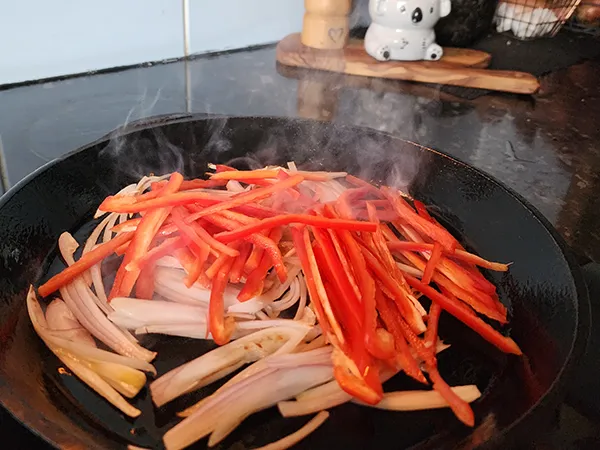 Adding sliced peppers to a skillet
