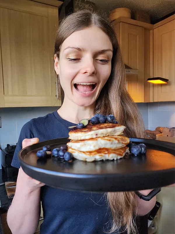 A woman is truing to bite a pancake from a plate she is holding in her hands